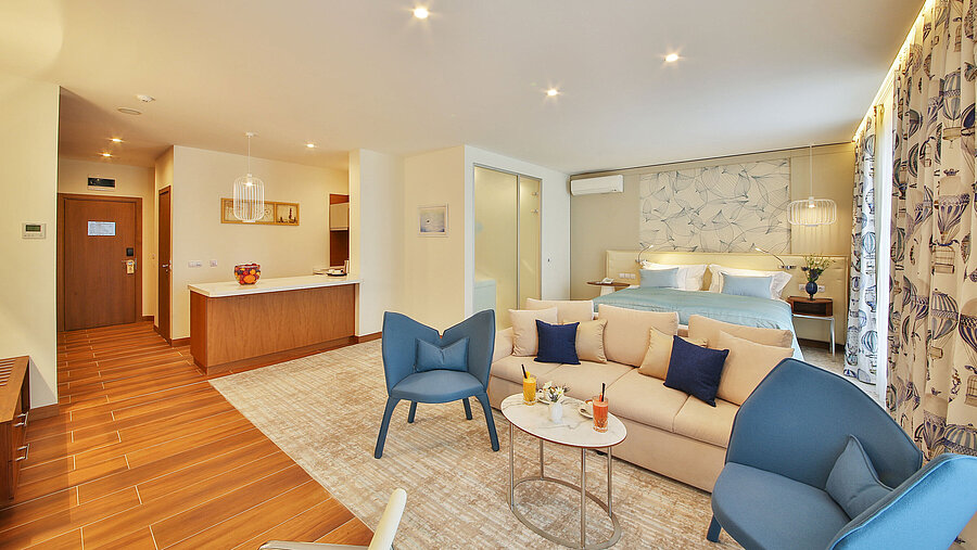 Spacious hotel room with sofa, chairs, bed area, kitchenette and modern design