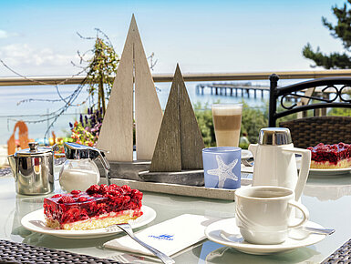 Coffee table with cake and hot drinks on the terrace of Maritim Seehotel Timmendorfer Strand with a sea view.