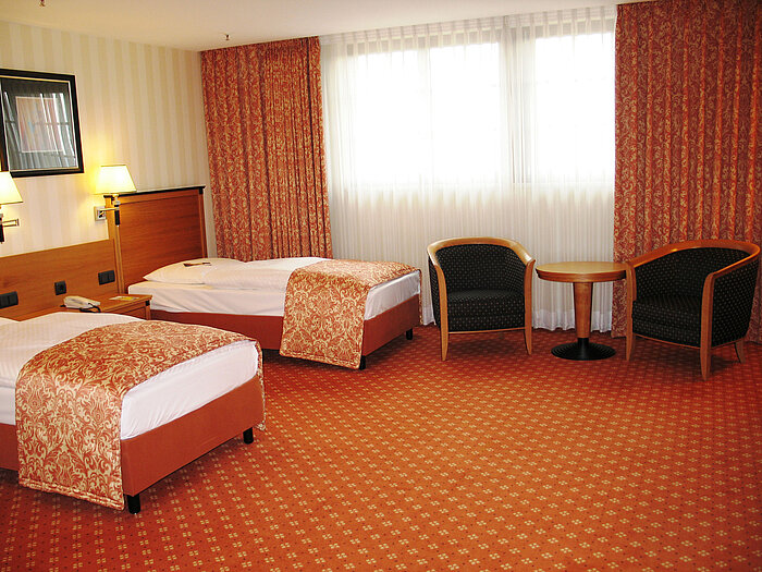 Bright twin room with two single beds, seating area and warm colours in the classic Maritim Hotel style