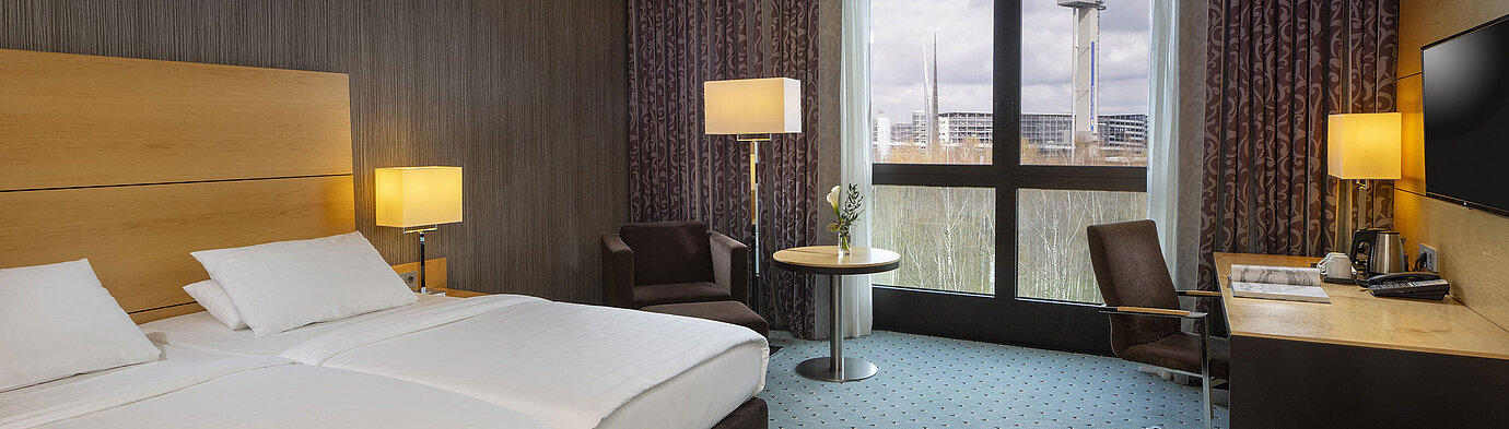 Classic room at Maritim Hotel Düsseldorf with double bed, desk, and panoramic window overlooking the surroundings.