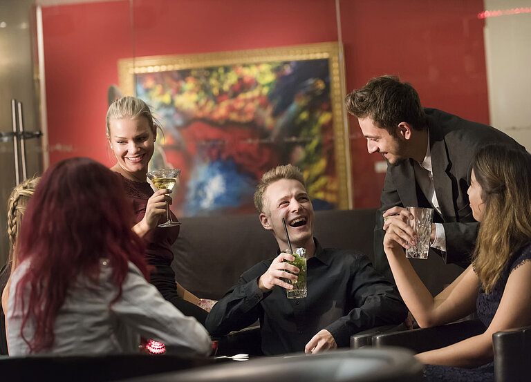 Group of guests enjoying cocktails and laughing at the bar of Maritim proArte Hotel Berlin.