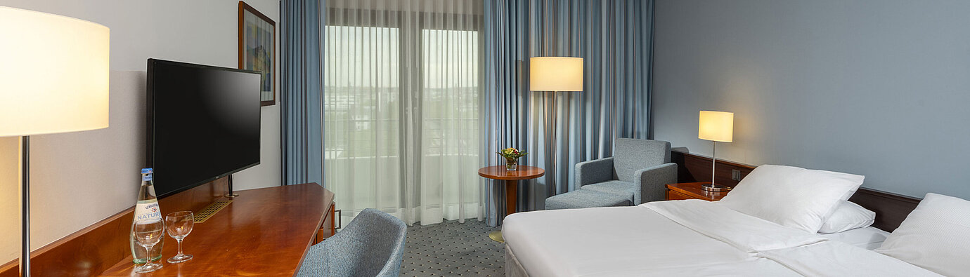 Classic double room at Maritim Hotel Darmstadt with desk, flat-screen TV, seating area, and large windows with curtains.