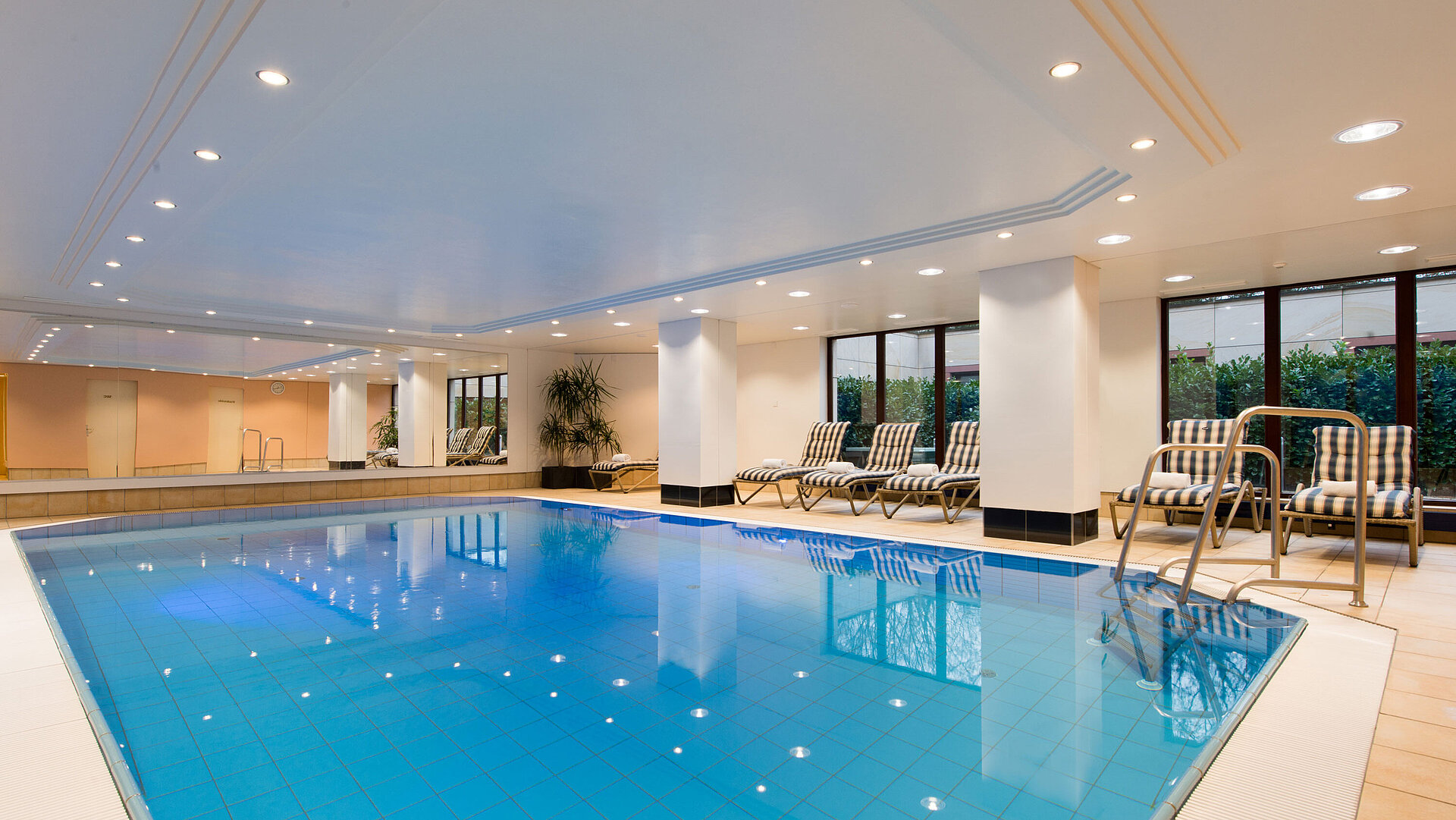Modern indoor pool at Maritim Hotel Fulda with lounge chairs, large windows, and a relaxing atmosphere.