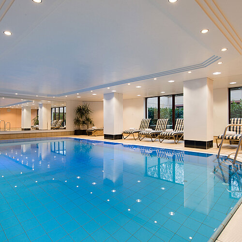 Modern indoor pool at Maritim Hotel Fulda with lounge chairs, large windows, and a relaxing atmosphere.