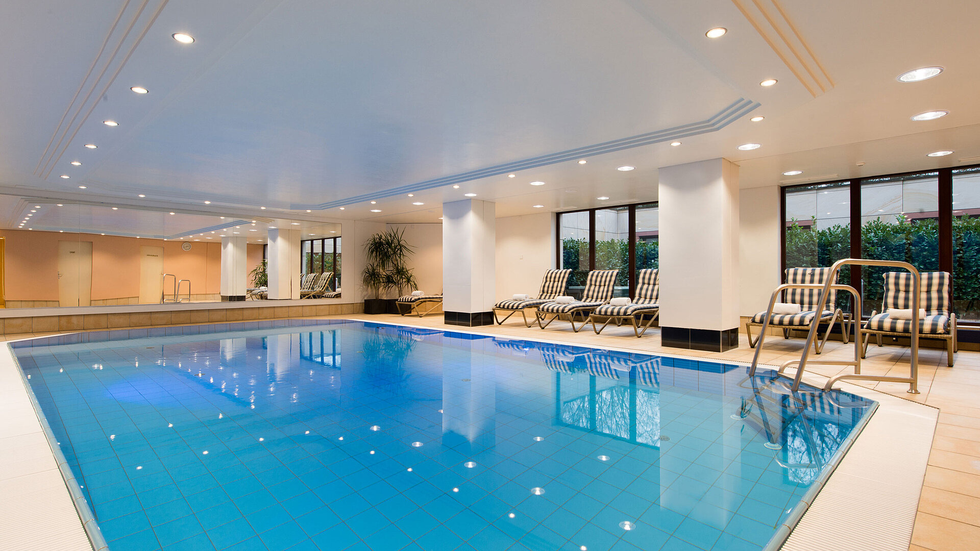 Modern indoor pool at Maritim Hotel Fulda with lounge chairs, large windows, and a relaxing atmosphere.