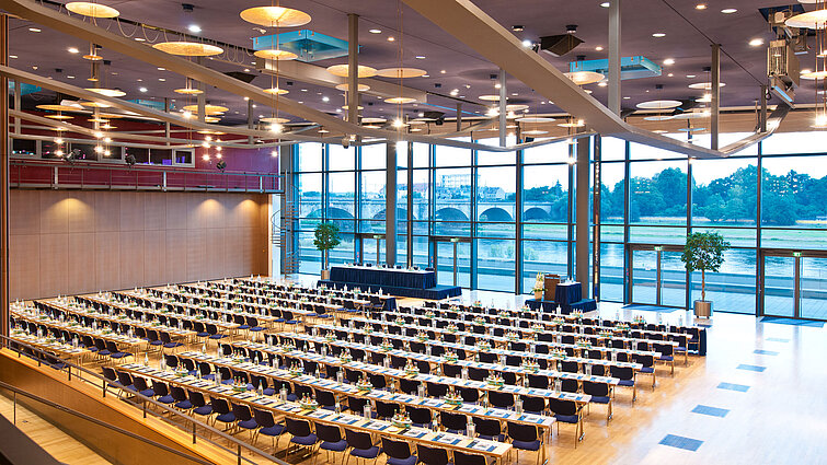 Large conference hall in Maritim Hotel Dresden with rows of blue chairs and a view of the Elbe River.