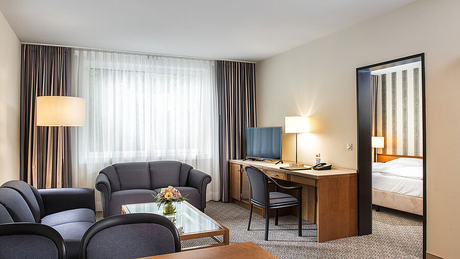 Living area with sofas, TV, desk and access to bedroom at Maritim Hotel Stuttgart