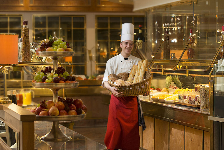 Baker with basket of bread at breakfast buffet at Maritim Hotel Stuttgart, surrounded by fresh fruit