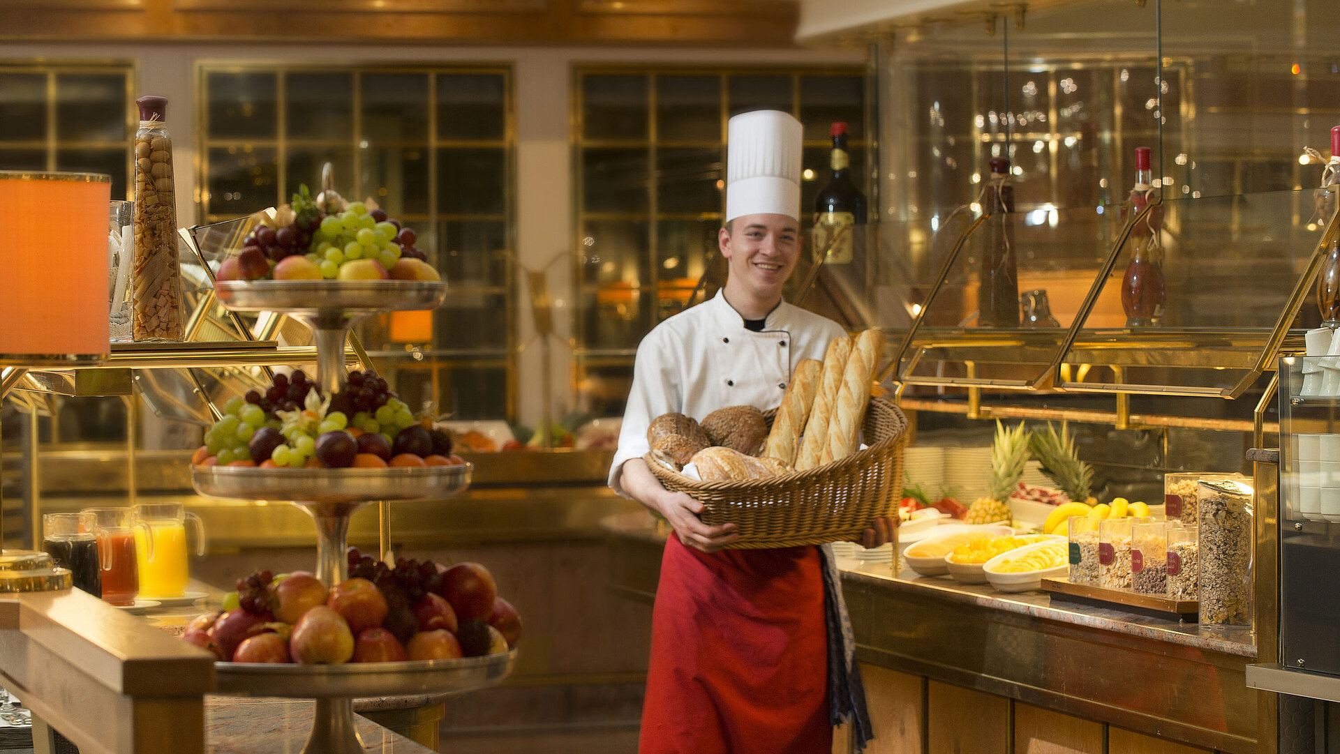 Baker with basket of bread at breakfast buffet at Maritim Hotel Stuttgart, surrounded by fresh fruit