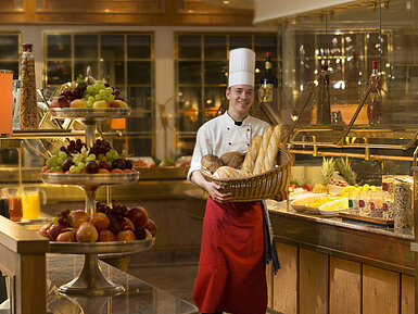 Baker with basket of bread at breakfast buffet at Maritim Hotel Stuttgart, surrounded by fresh fruit