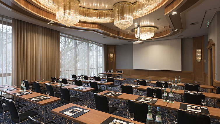 Elegant meeting room with theatre seating, chandeliers and projector screen at Maritim Hotel Ulm.