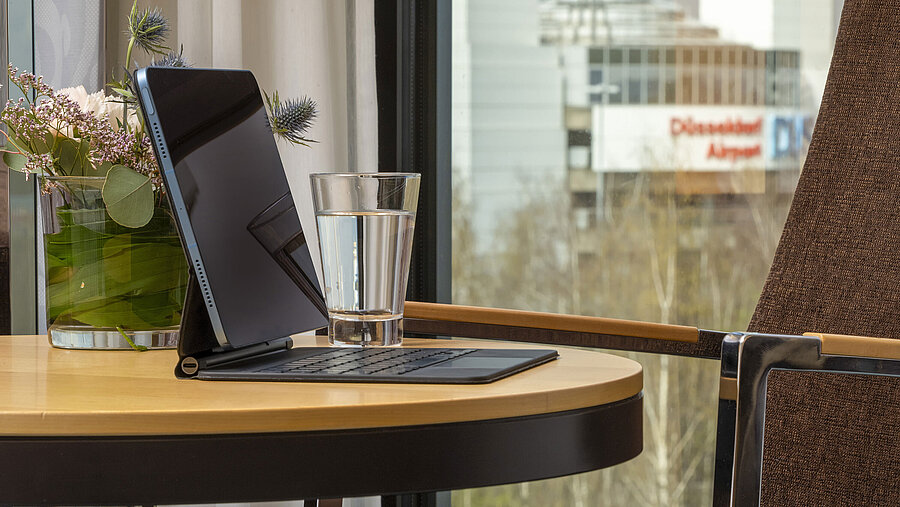 Close-up of a table at Maritim Hotel Düsseldorf with a tablet, glass of water, and view of Düsseldorf Airport.
