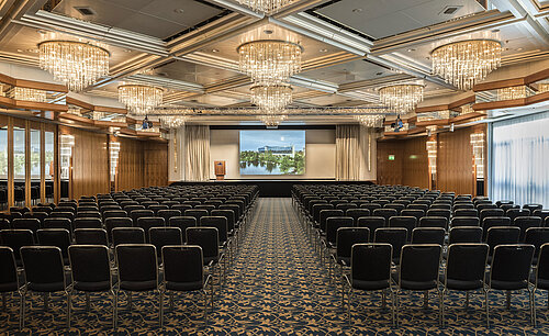 Elegant event hall with crystal chandeliers, row seating, and a large stage at Maritim Hotel Hannover.