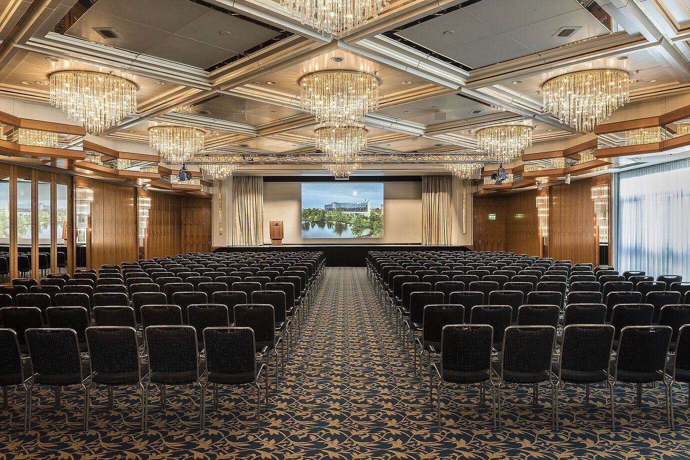 Elegant event hall with crystal chandeliers, row seating, and a large stage at Maritim Hotel Hannover.