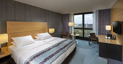 Modern superior room at Maritim Hotel Düsseldorf with a large bed, desk, and city view.