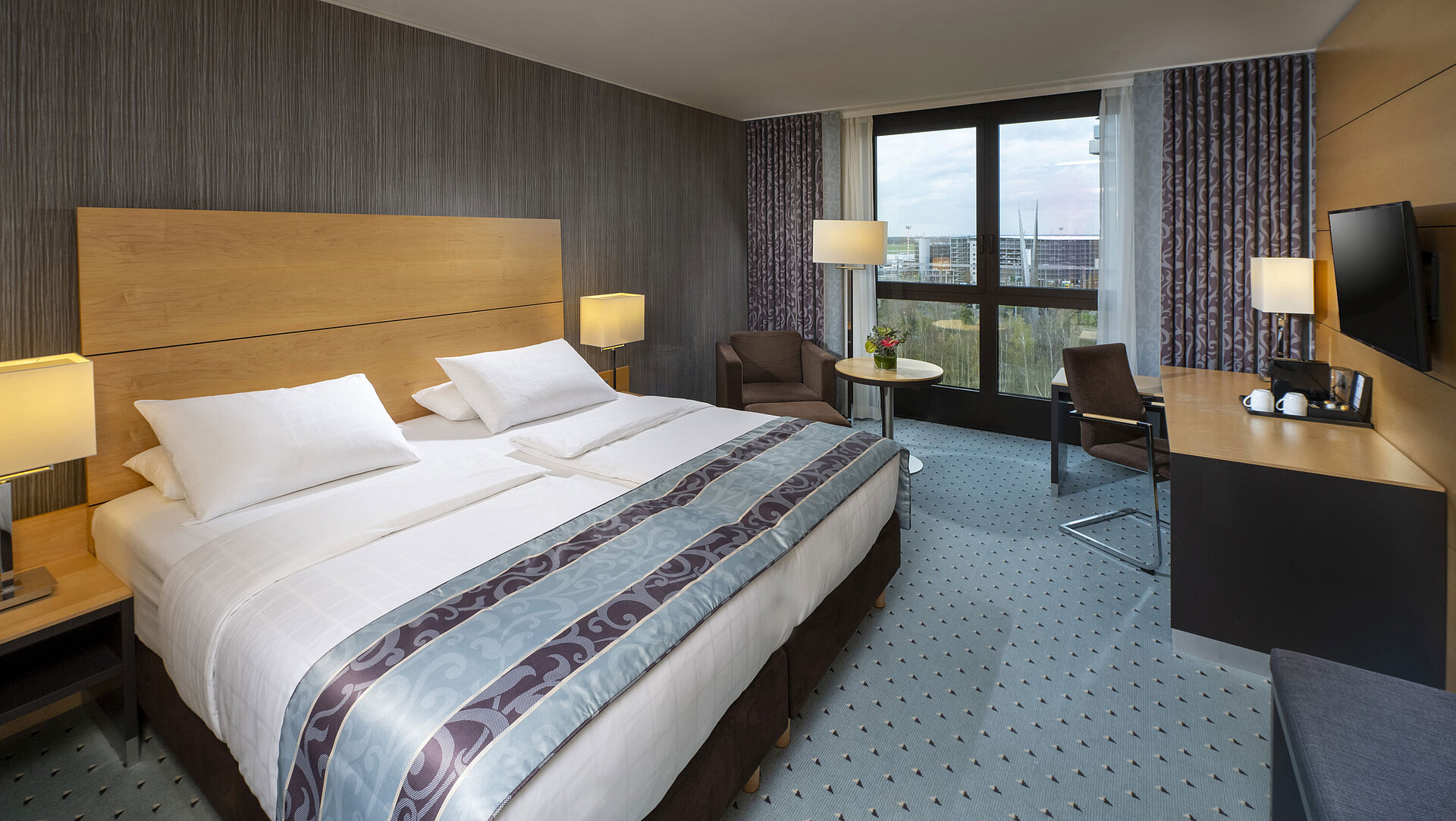 Modern superior room at Maritim Hotel Düsseldorf with a large bed, desk, and city view.