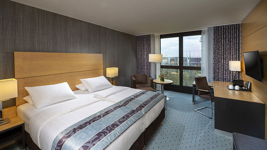 Modern superior room at Maritim Hotel Düsseldorf with a large bed, desk, and city view.