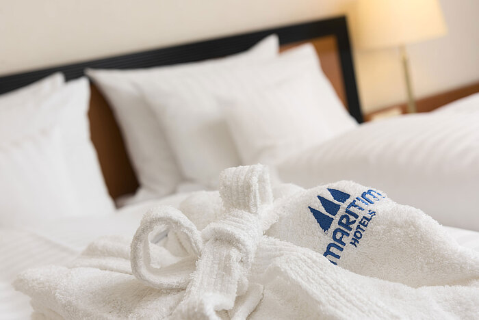 Soft bathrobe with Maritim logo on the bed at Maritim Hotel Bad Salzuflen
