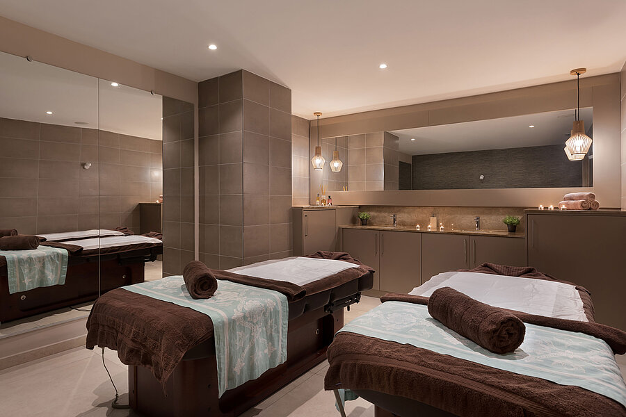 Modern wellness room with two massage tables, warm lighting and a relaxing spa atmosphere