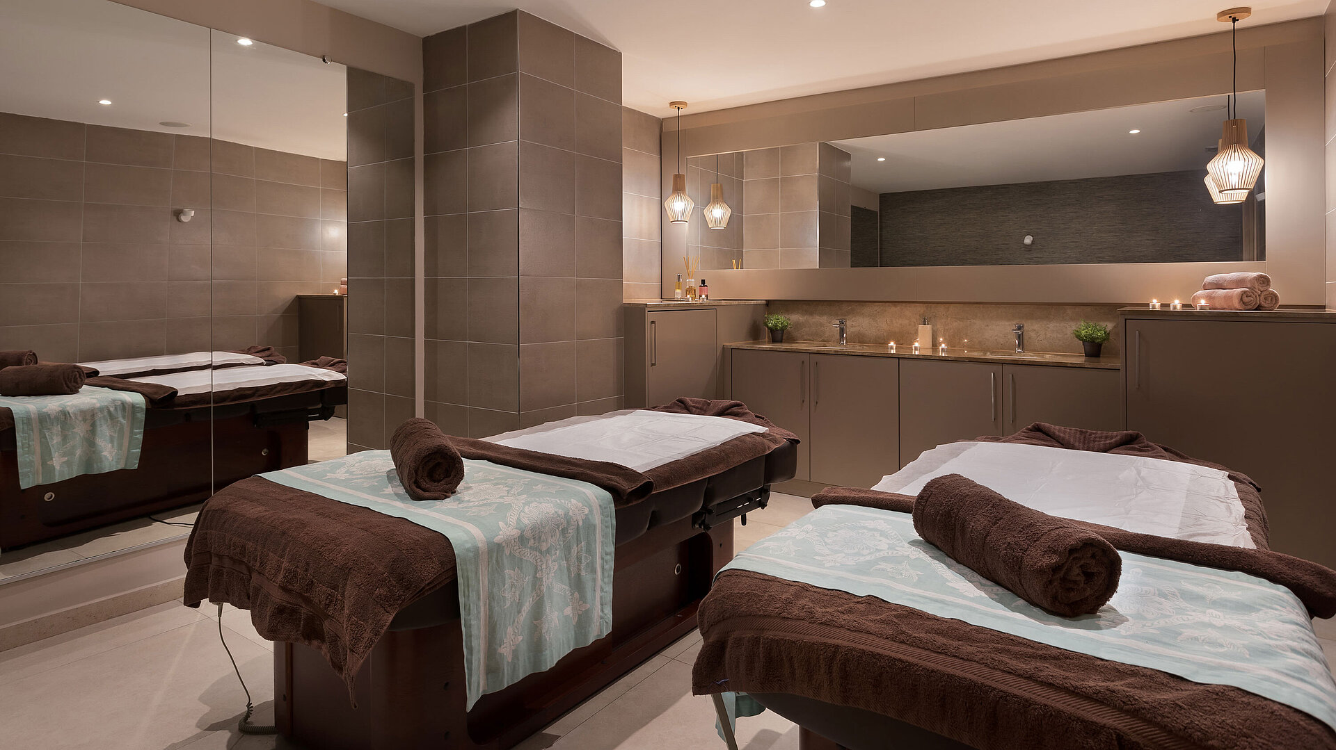 Modern wellness room with two massage tables, warm lighting and a relaxing spa atmosphere