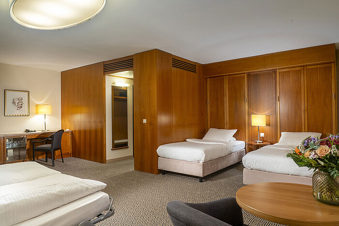 Bright family room with three beds, desk and elegant wooden walls at the Maritim Hotel Stuttgart