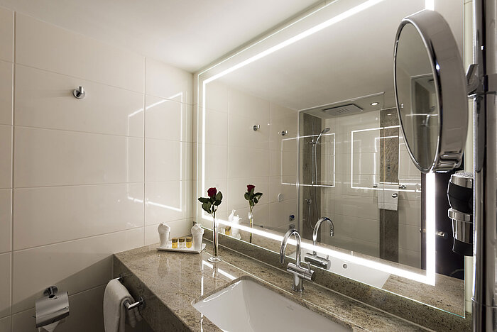 Modern bathroom at Maritim Hotel Würzburg with large illuminated mirror and granite countertop.