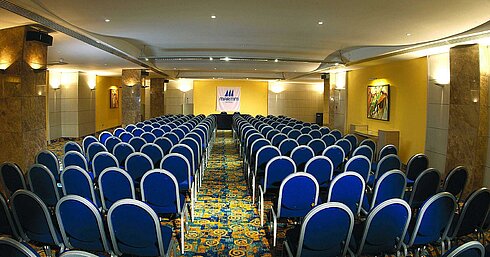 Bright conference room with theatre seating, stage and Maritim Hotels logo for meetings and events