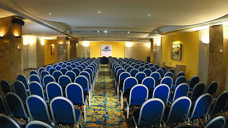 Bright conference room with theatre seating, stage and Maritim Hotels logo for meetings and events