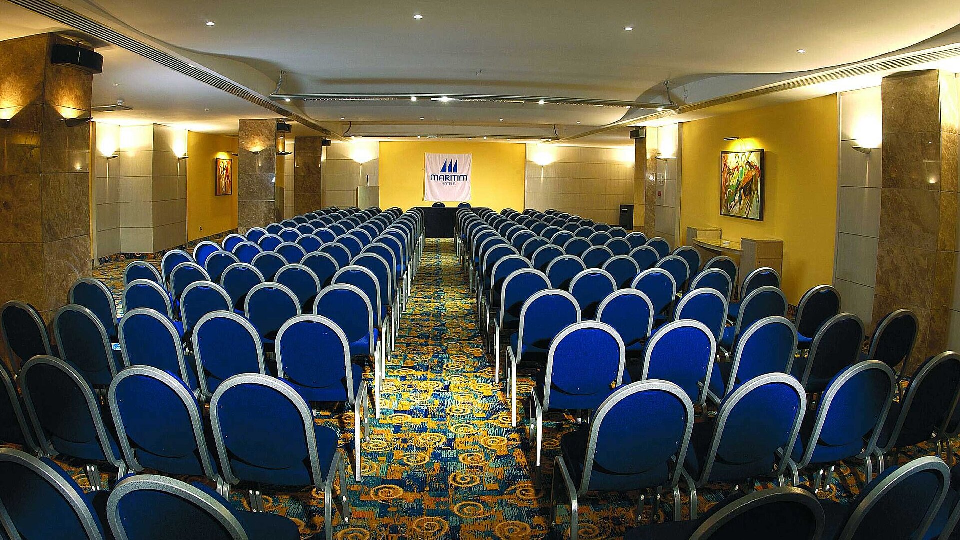Bright conference room with theatre seating, stage and Maritim Hotels logo for meetings and events