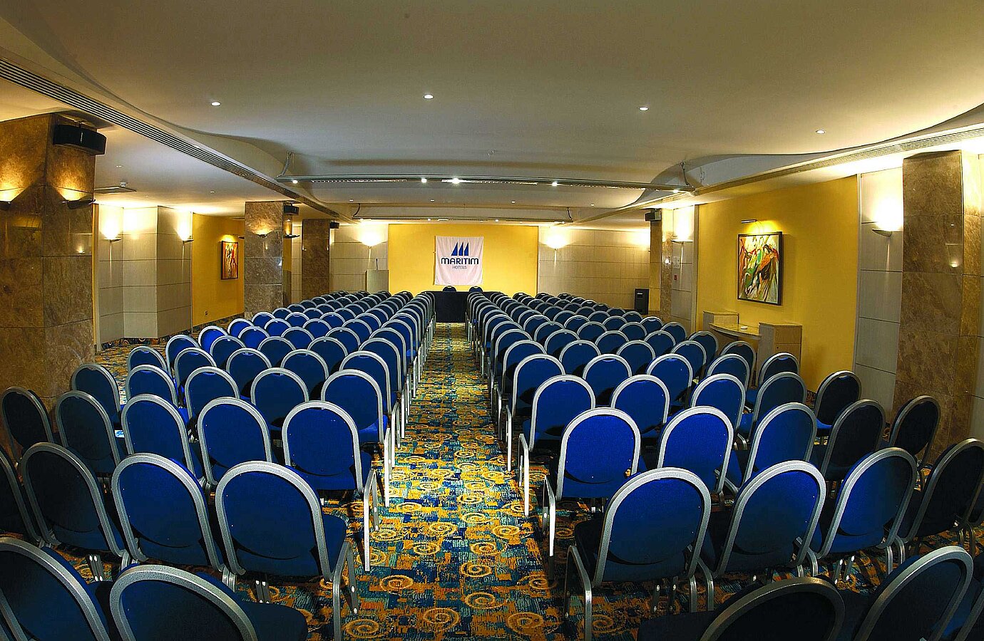 Bright conference room with theatre seating, stage and Maritim Hotels logo for meetings and events