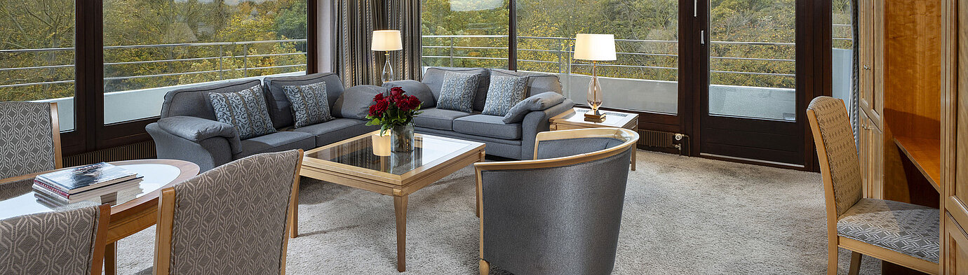 Living area of the Grand Suite at Maritim Hotel Kiel with large windows, stylish decor, and a view of greenery.