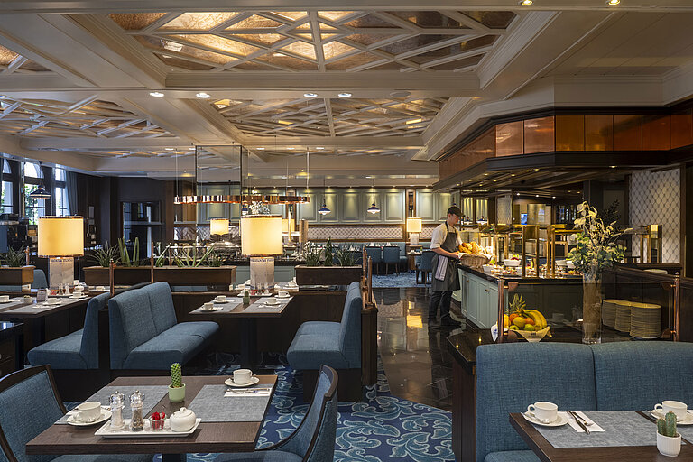Restaurant at the Maritim Hotel Darmstadt with set tables, buffet area, and elegant lighting under an artistic ceiling.