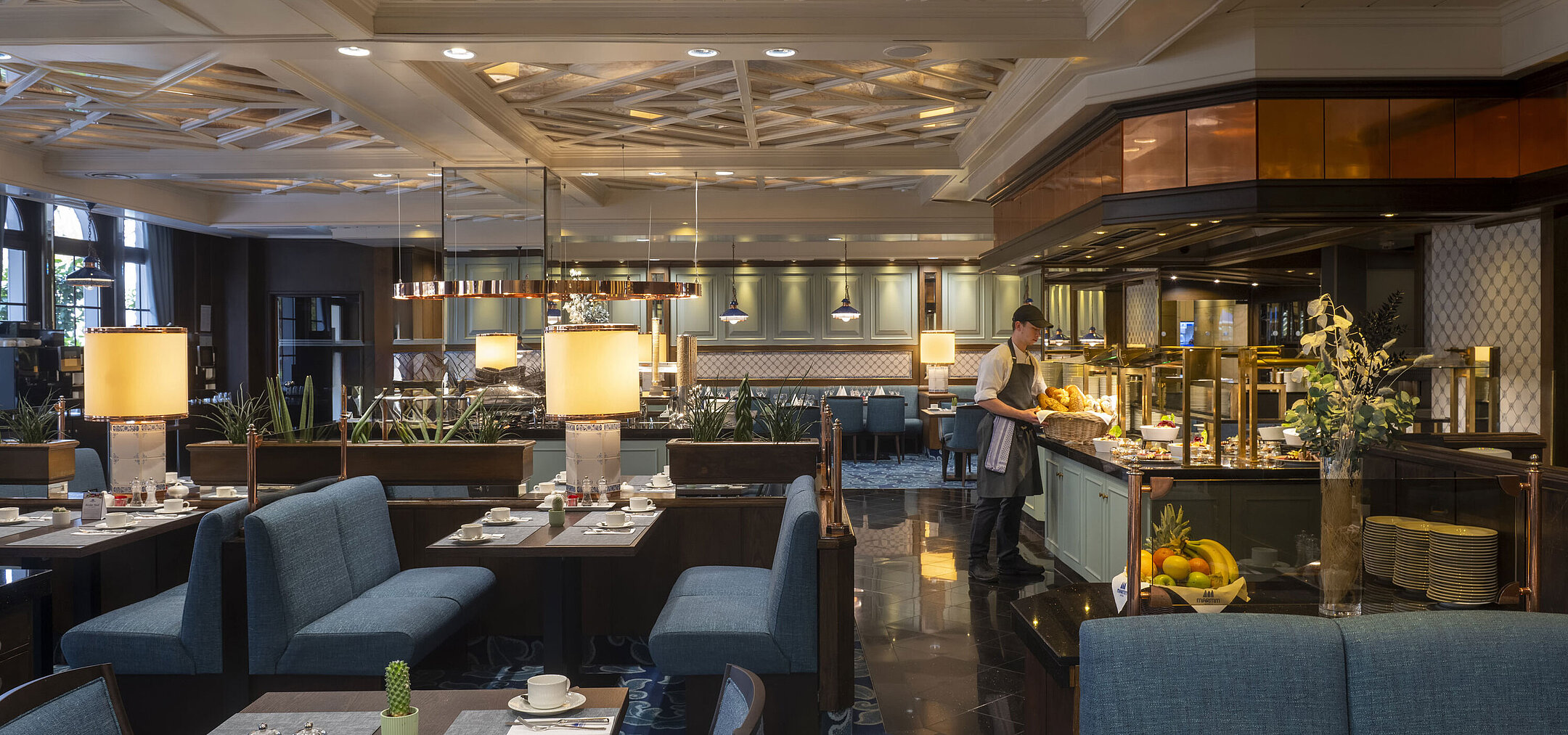 Restaurant at the Maritim Hotel Darmstadt with set tables, buffet area, and elegant lighting under an artistic ceiling.