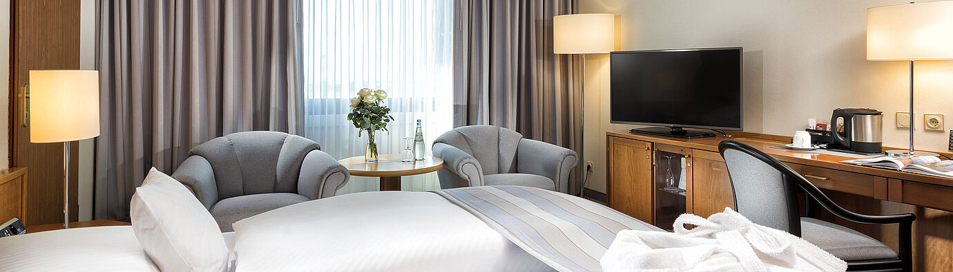 Superior double room with stylish furnishings, cozy seating area, water bottles and a bathrobe on the bed.