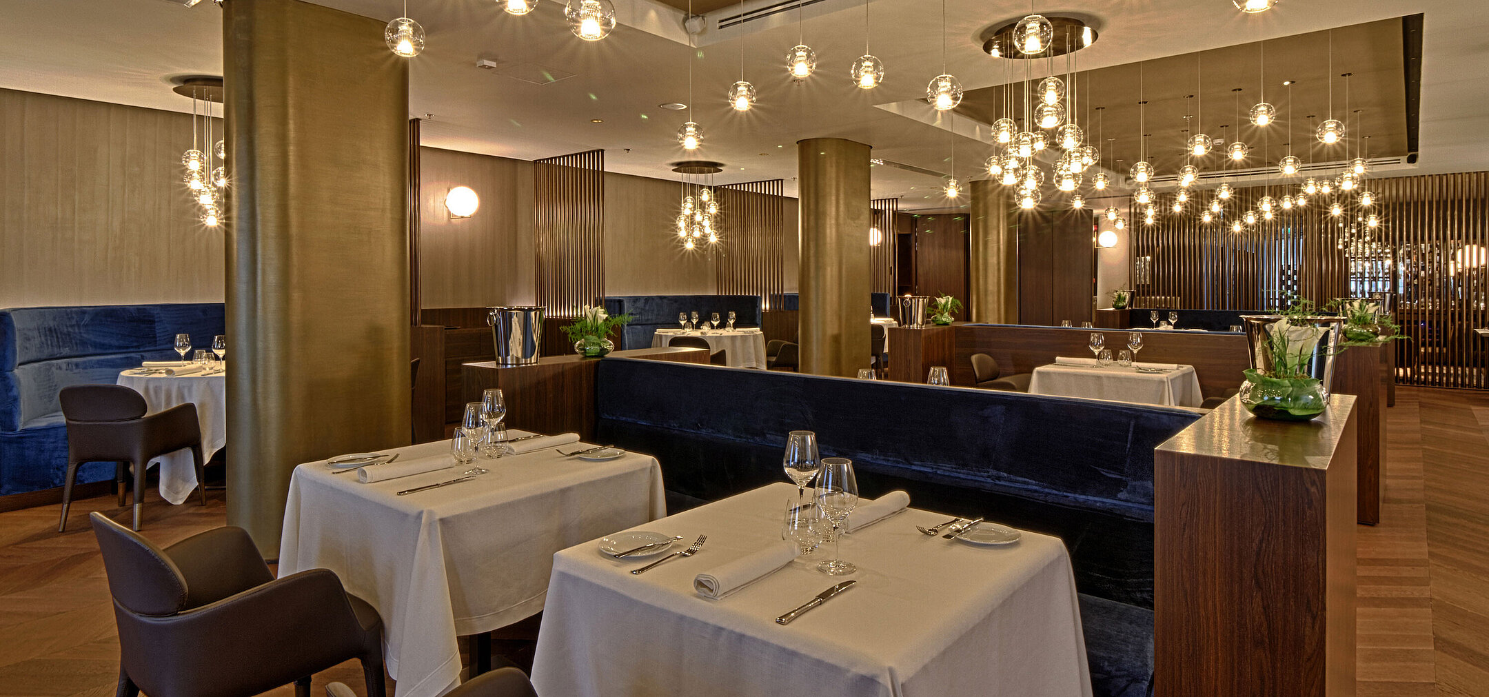 Spacious restaurant with elegant lighting, wooden floor and set tables at Maritim Hotel Plaza Tirana