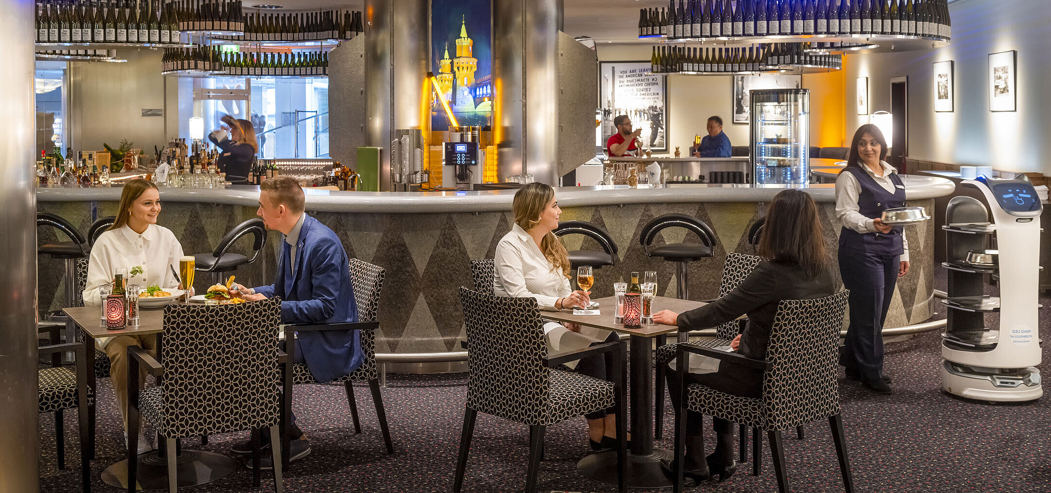 Guests dining at the bar of the Maritim proArte Hotel Berlin, surrounded by modern facilities and a service robot.