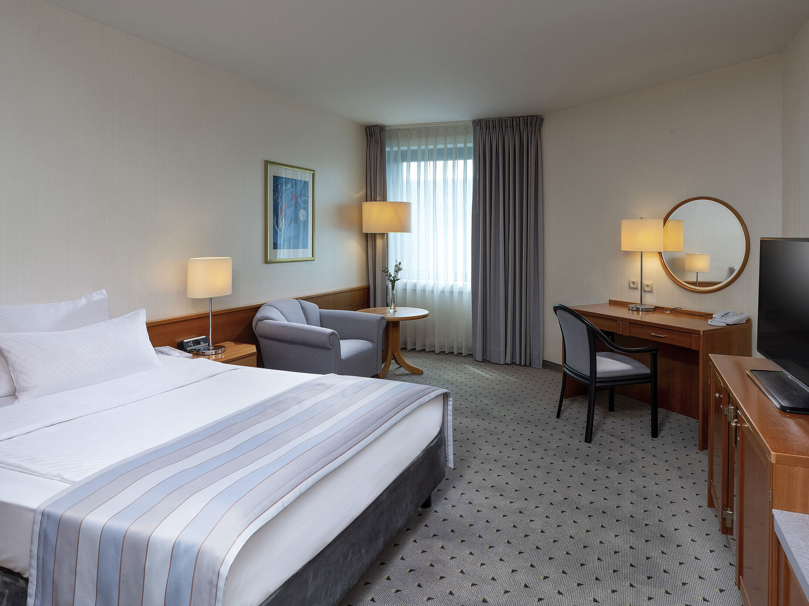 Cozy classic room with a large bed, desk, TV, and elegant decor at Maritim Hotel Hannover.
