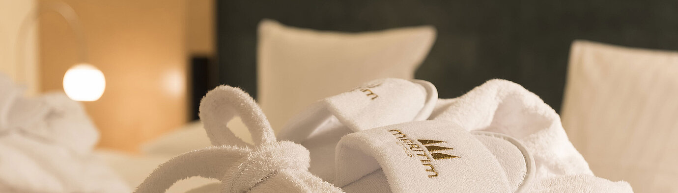 A fluffy bathrobe and slippers with Maritim logo on a bed at the Maritim proArte Hotel Berlin.