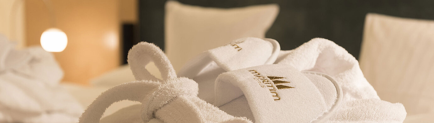 A fluffy bathrobe and slippers with Maritim logo on a bed at the Maritim proArte Hotel Berlin.