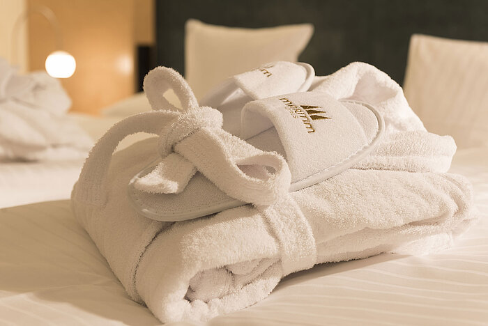 A fluffy bathrobe and slippers with Maritim logo on a bed at the Maritim proArte Hotel Berlin.