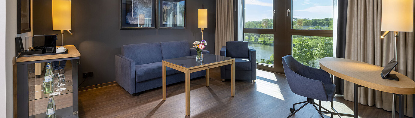 Bright suite with seating area, large window, and nature view at Maritim Hotel Ingolstadt.