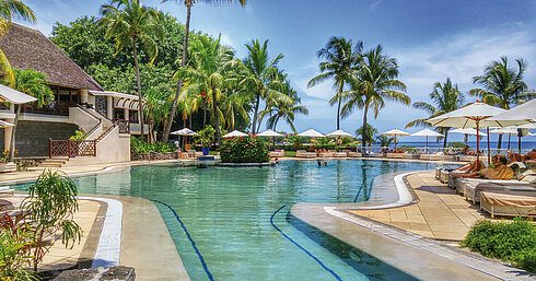 Large hotel pool with palm trees, sun loungers and sea views in a tropical holiday setting