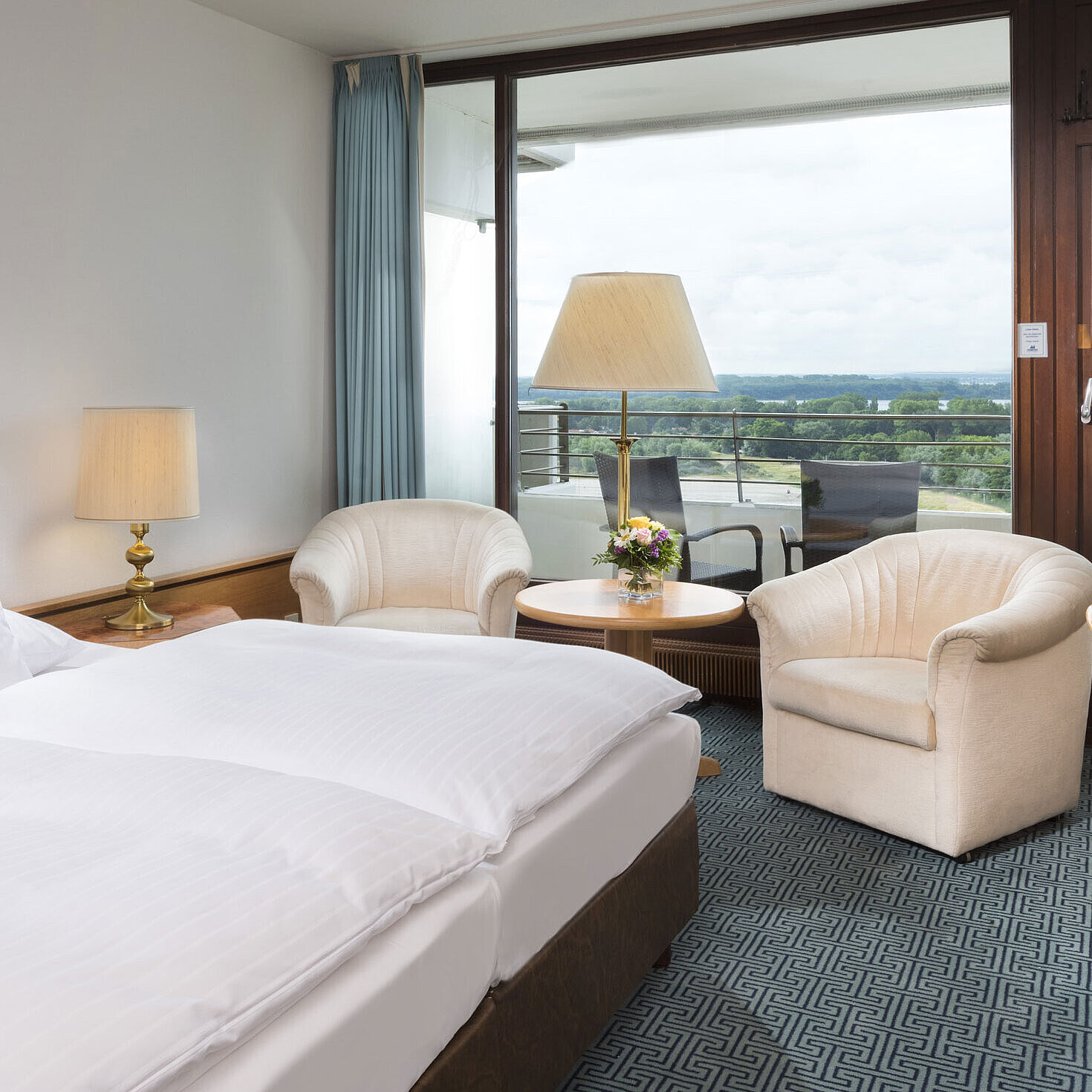 Double room with seating area, desk and balcony overlooking green landscape in Travemünde