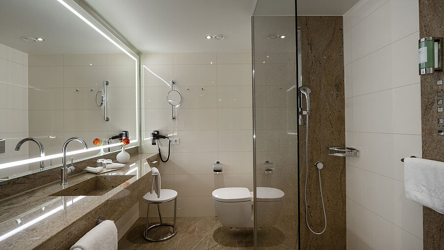 Bathroom at Maritim Hotel Ingolstadt with glass shower, large mirror, and stylish design.