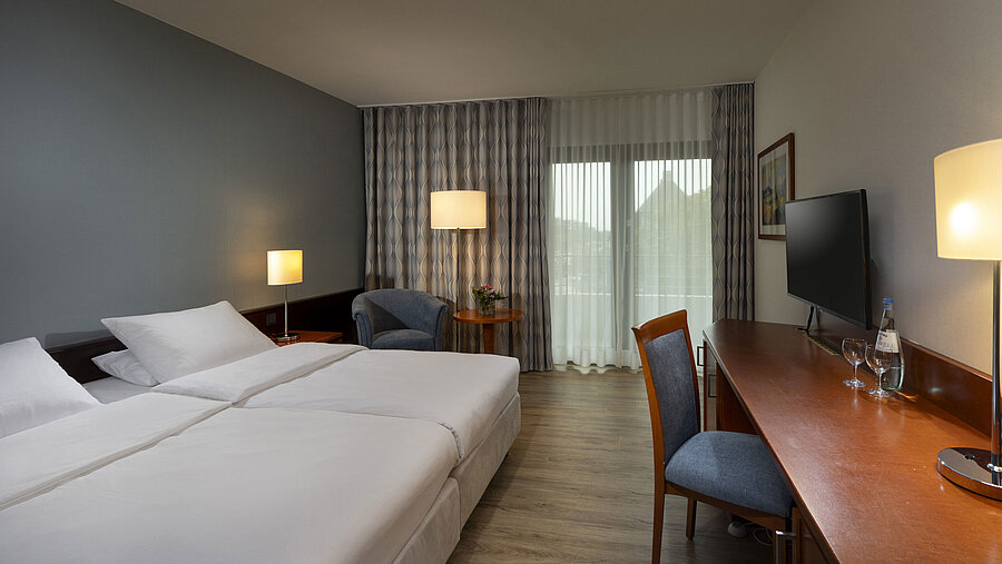 Modernly furnished allergy-friendly room at Maritim Hotel Darmstadt with wooden floor, double bed, desk, and balcony access.