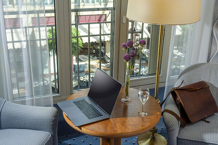 Classic room at the Maritim Hotel Cologne with a laptop on the table, a glass of water, a leather bag, and flowers in a vase.