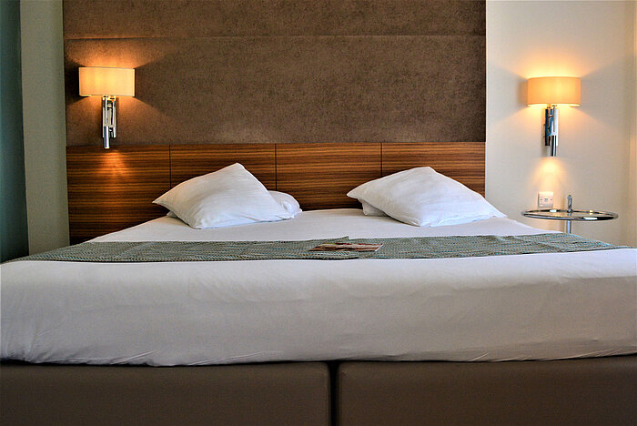 Comfortable double bed with dark headboard, reading lamps and high-quality bedding