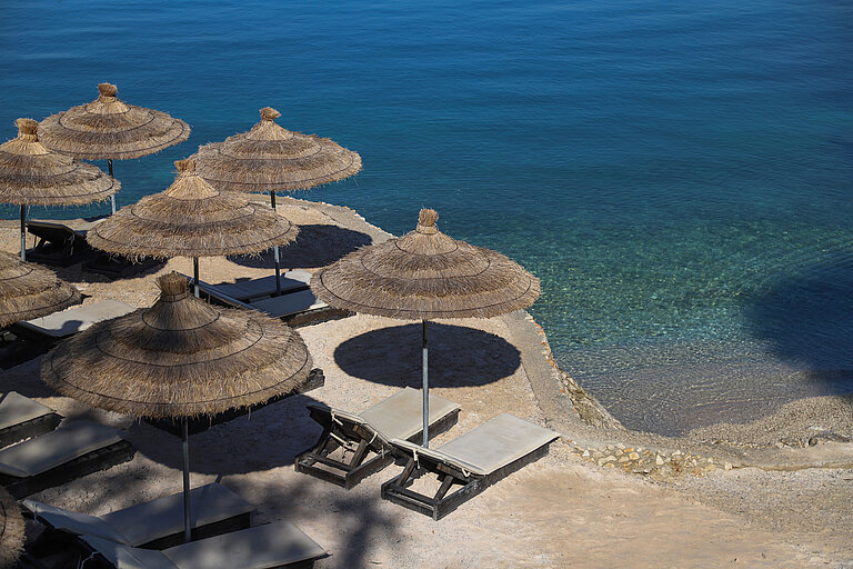 Beach area at Maritim Resort Marina Bay with straw parasols, loungers and crystal-clear sea