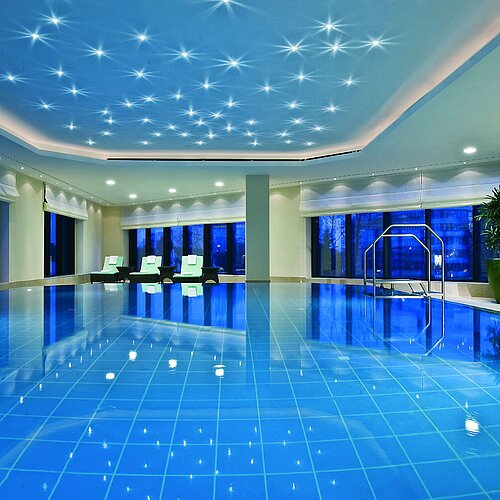 Illuminated indoor pool at Maritim Hotel Düsseldorf with modern loungers and panoramic windows, perfect for relaxation.