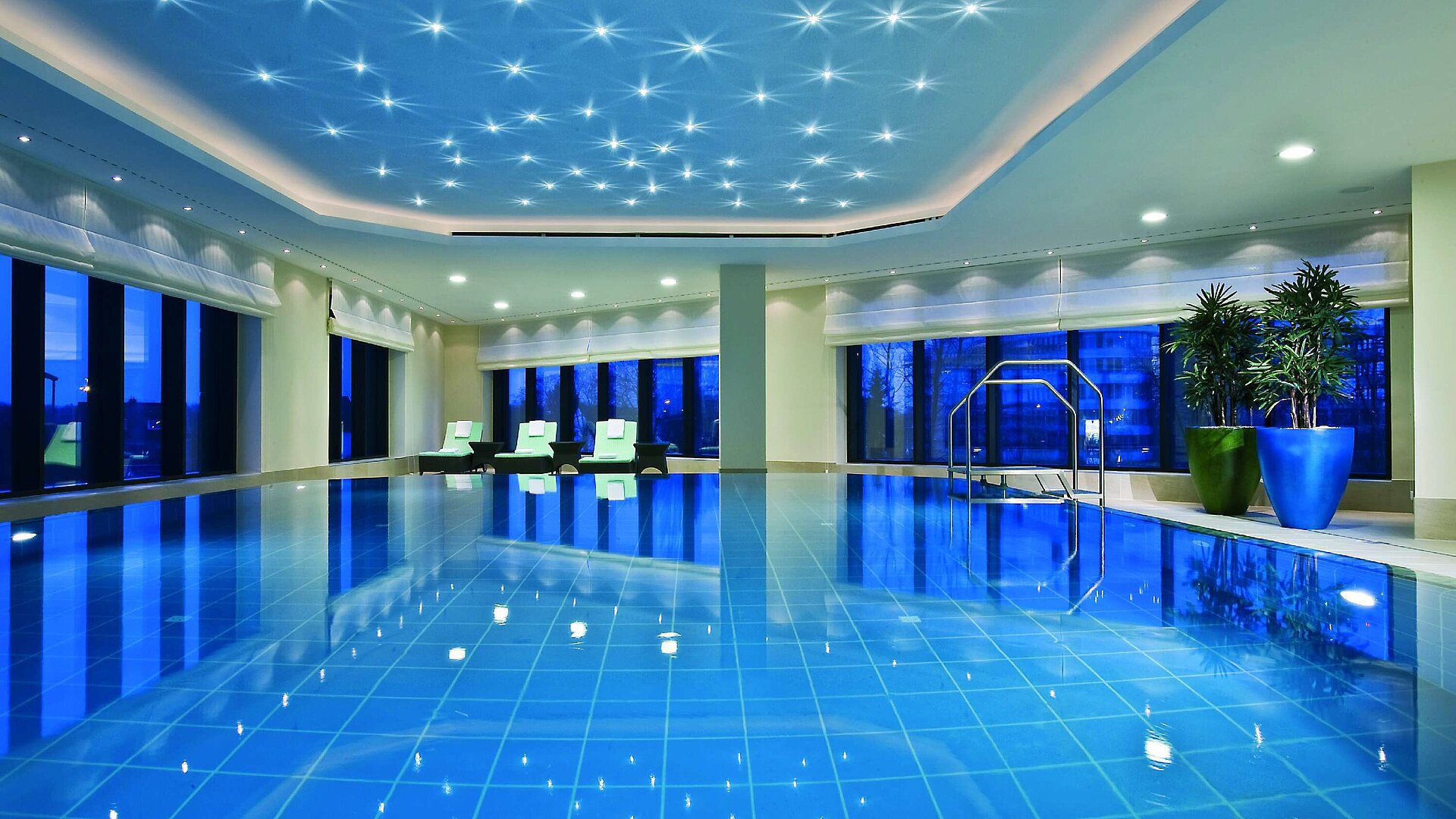Illuminated indoor pool at Maritim Hotel Düsseldorf with modern loungers and panoramic windows, perfect for relaxation.